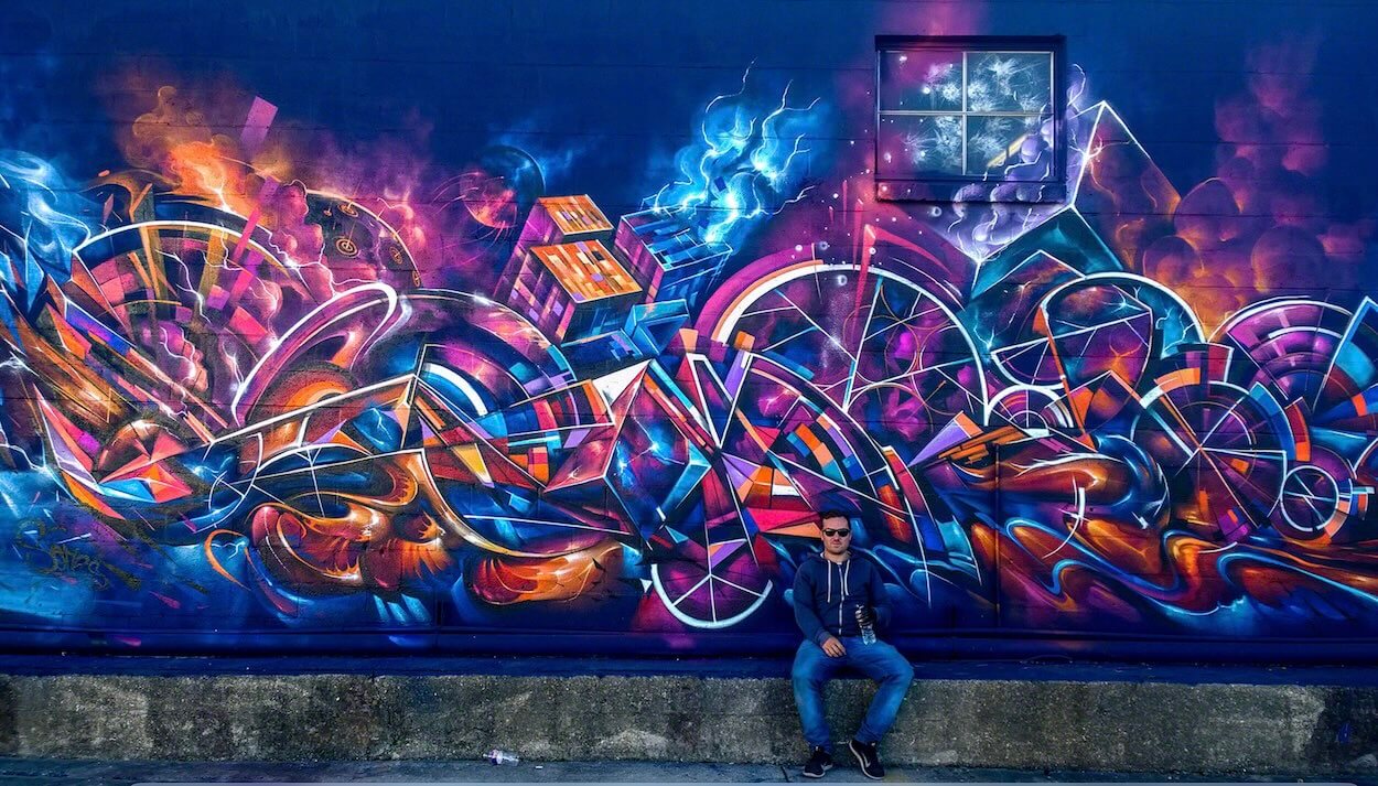 l'artiste graffeur Sofles pose devant sa pièce