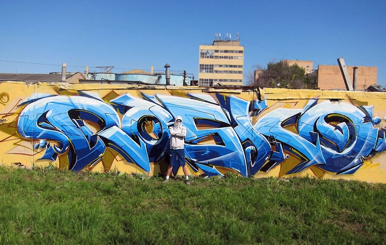 le graffeur RASKO pose devant son lettrage